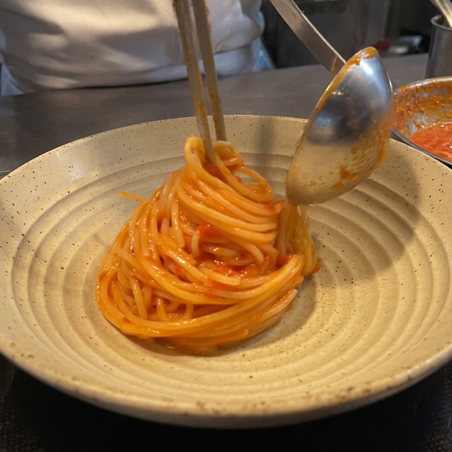 Uno chef che usa pinze e un mestolo di metallo per arrotolare gli spaghetti al pomodoro in un bel nido su un piatto di ceramica rustico.