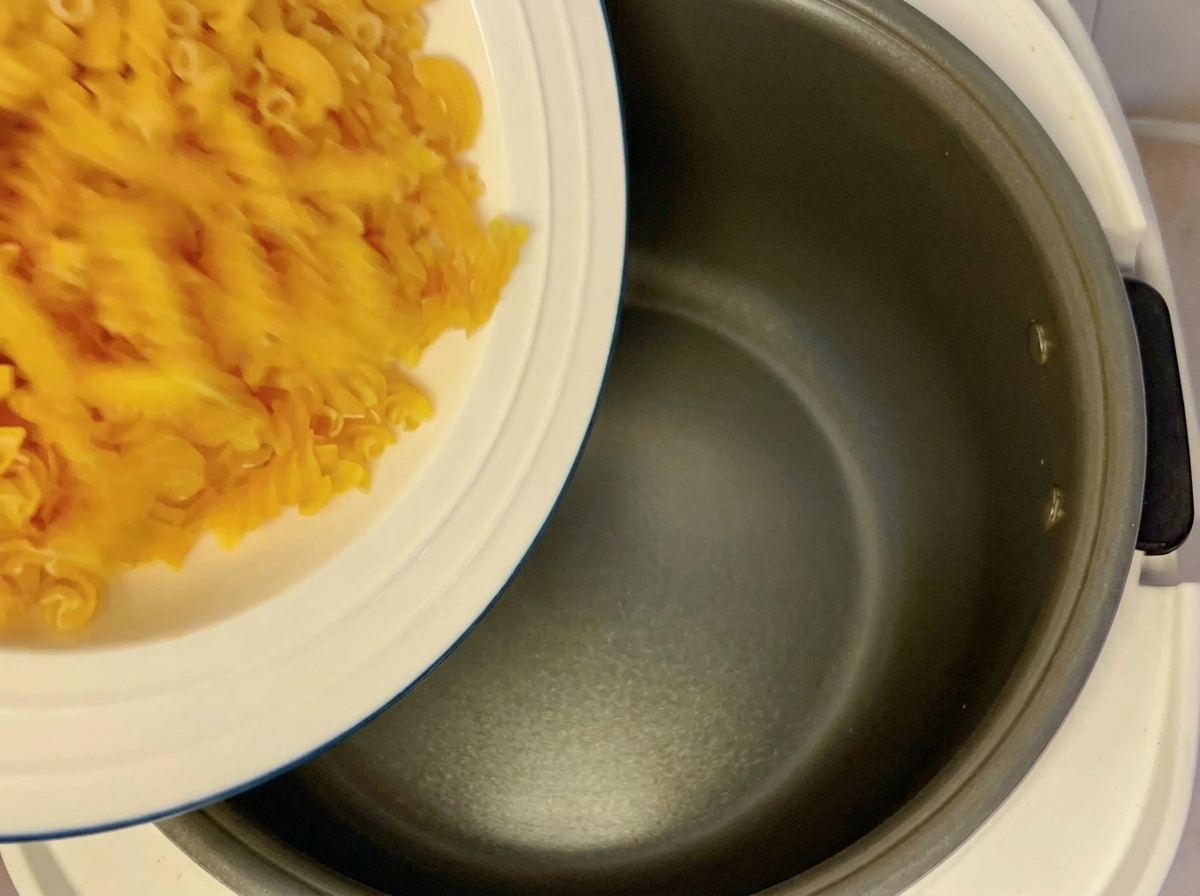 Fusilli secchi versati da un piatto bianco in un cuociriso vuoto.