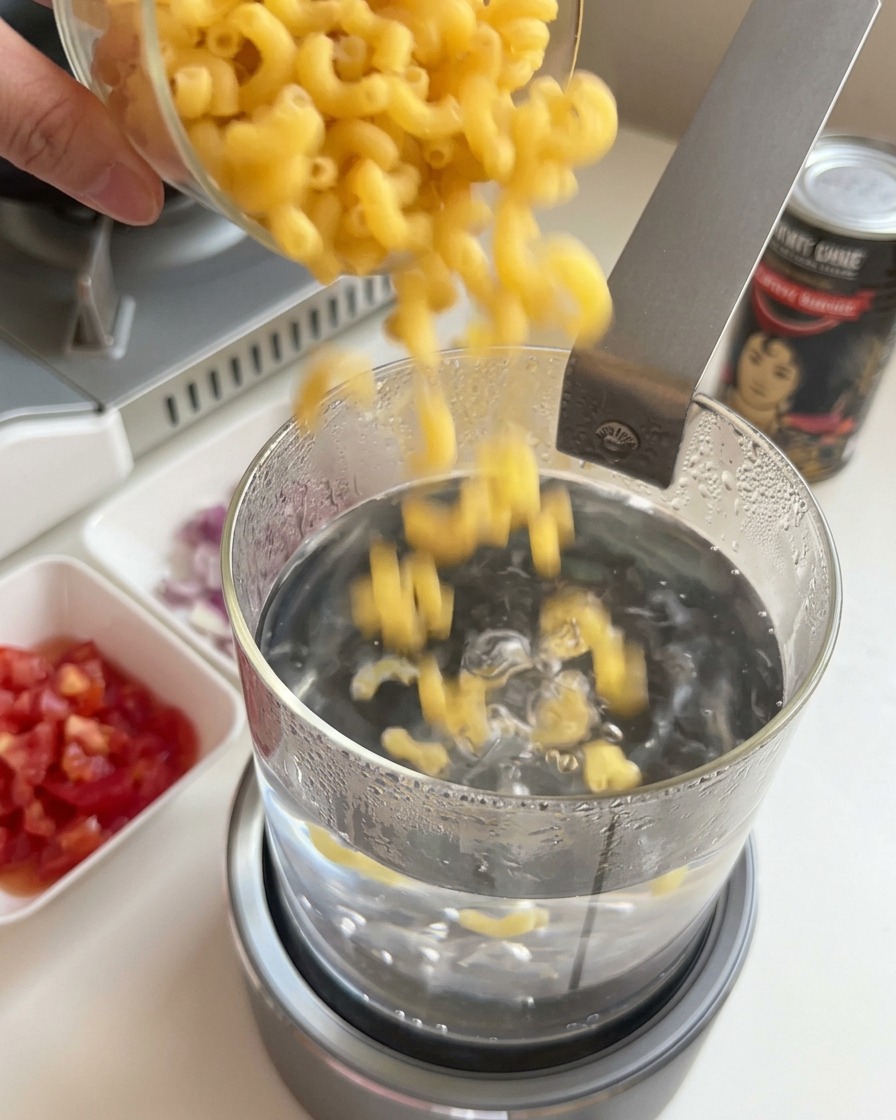 Maccheroni secchi versati in una pentola di vetro con acqua bollente.