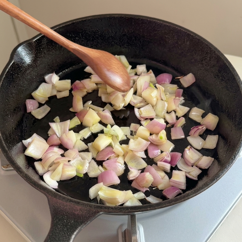 Cipolle tritate che soffriggono in una padella di ghisa con un cucchiaio di legno.