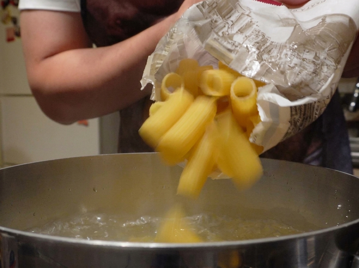 Rigatoni secchi che cadono da un sacchetto di carta in una pentola dacqua bollente.