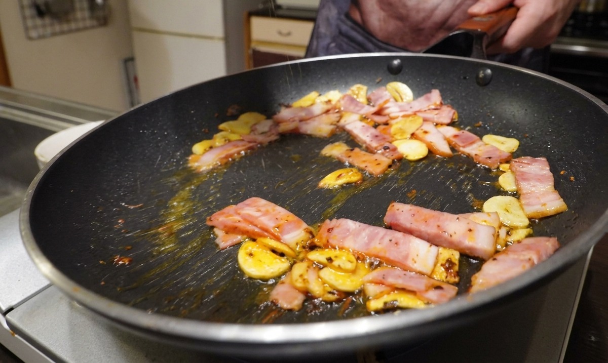 Pancetta a fette, aglio e peperoncino che sfrigolano in padella conditi con pepe nero macinato fresco.