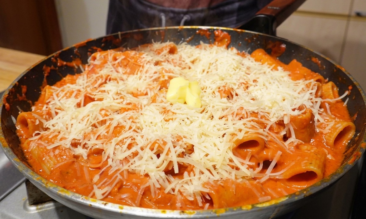 Un cubetto di burro giallo su una montagna di parmigiano e rigatoni in una padella calda.