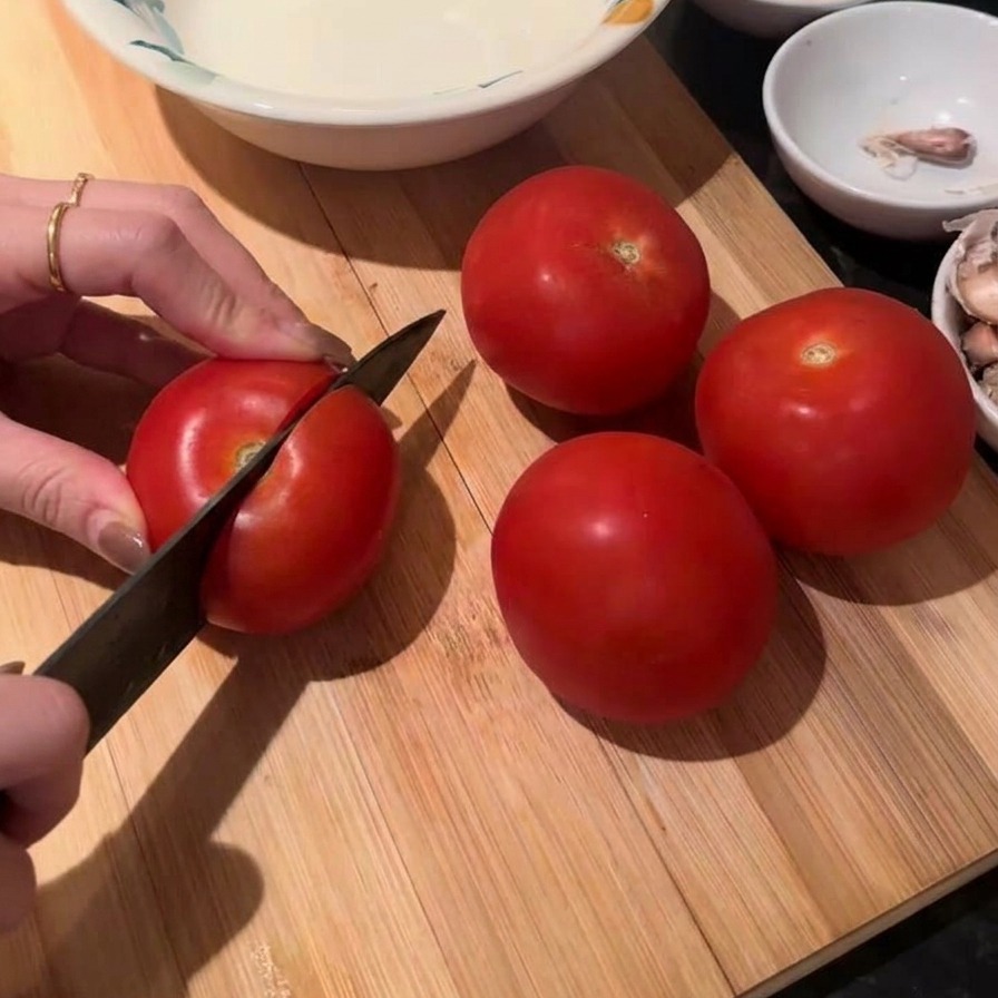 Mani che usano un coltello da chef per tagliare un pomodoro rosso fresco su un tagliere di legno.