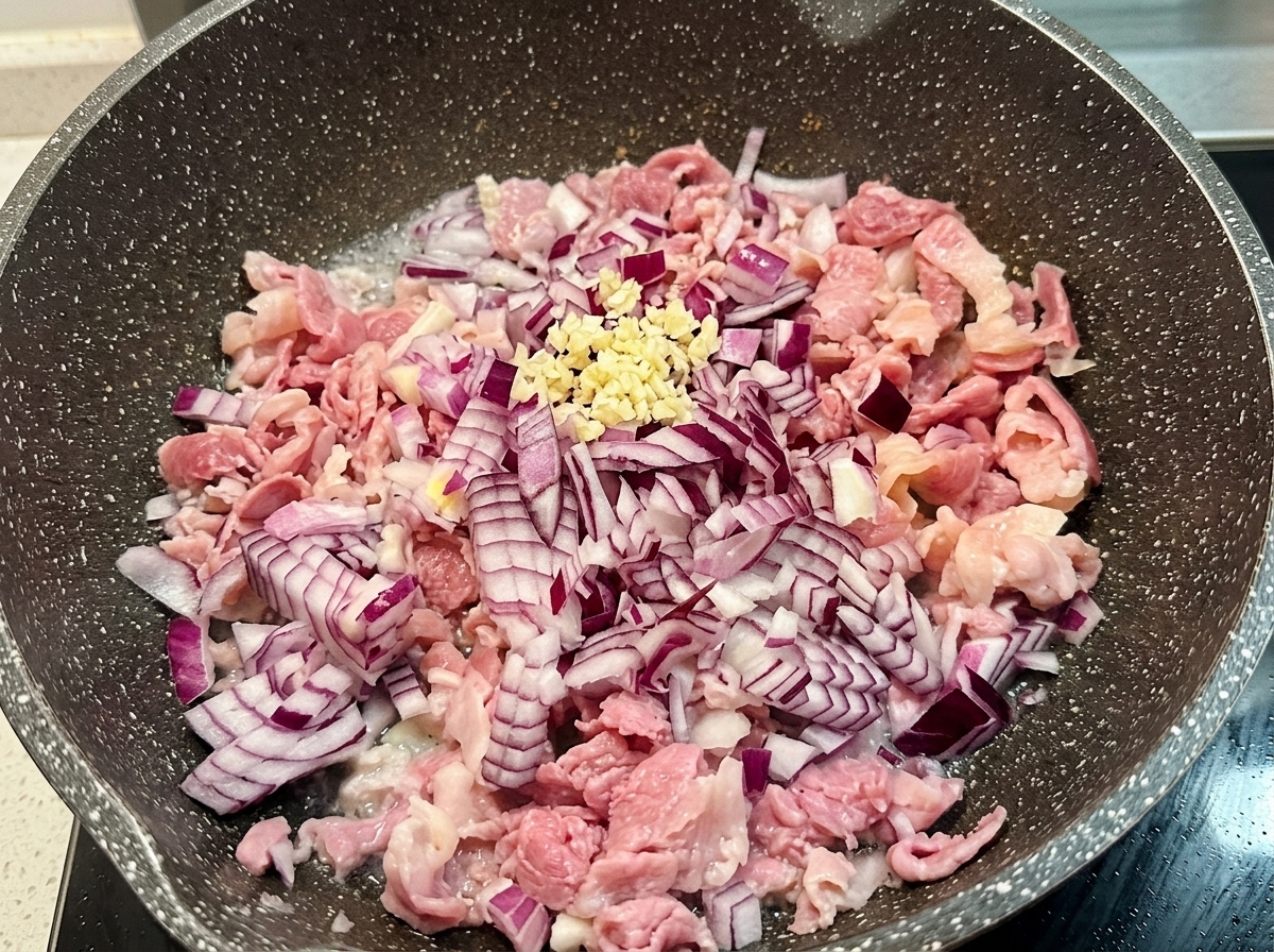 Una piccola quantità di aglio tritato fresco sopra la cipolla rossa e il bacon in padella.