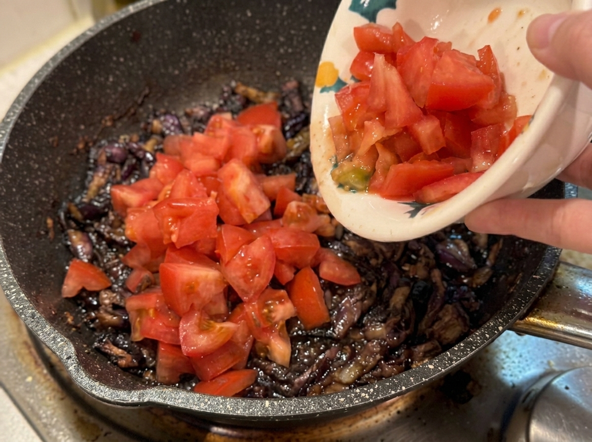 Una mano che versa pomodori freschi a cubetti in una padella calda con bacon e aromi.