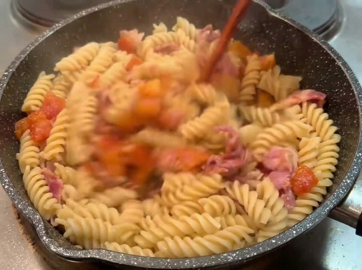 Fusilli cotti saltati in padella con un sugo corposo di pomodoro e bacon usando un utensile di legno.