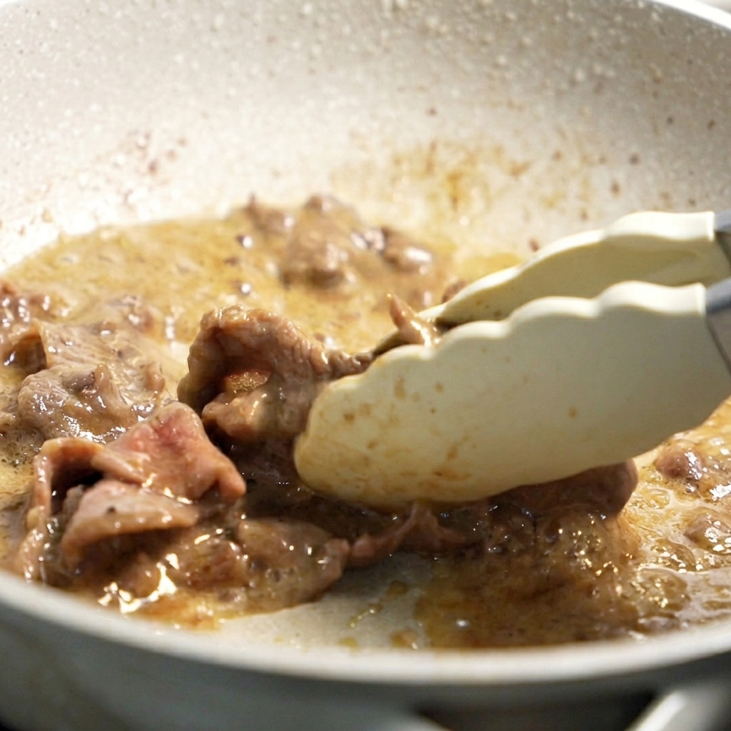 Pinze che tolgono le fettine di manzo dorate dalla padella calda.