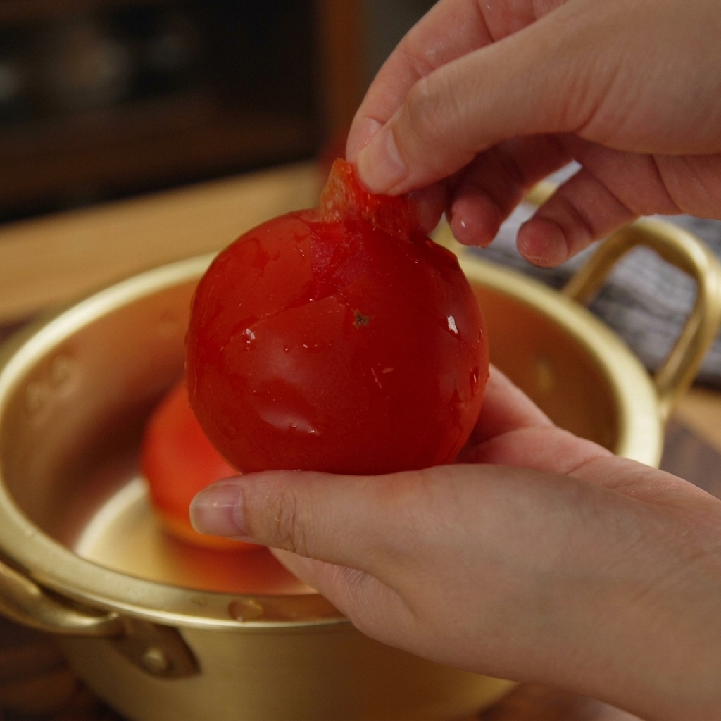 Mani che rimuovono la buccia da un pomodoro rosso sopra una ciotola.