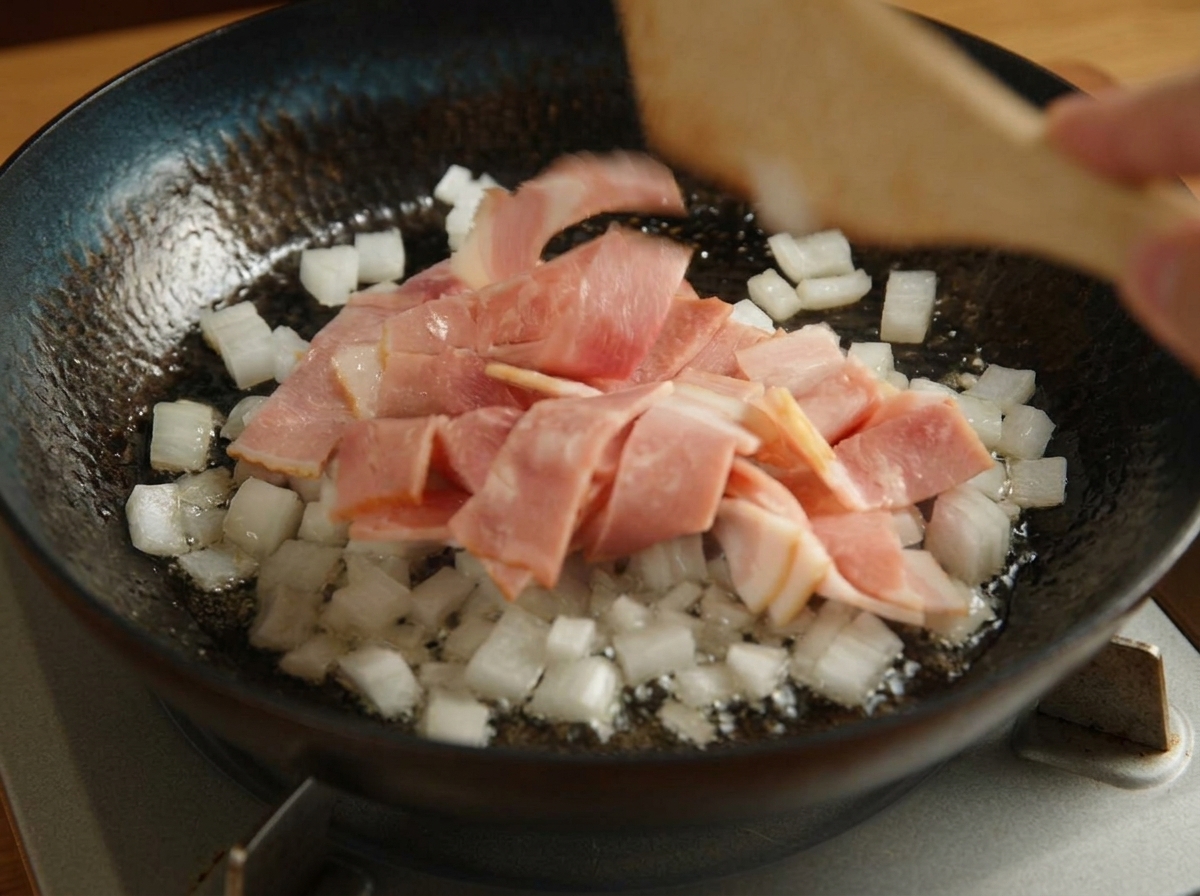 Spatola di legno che mescola bacon e cipolle in una padella nera sul fuoco.