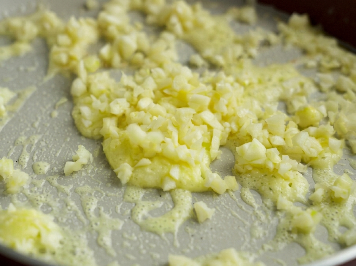 Aglio tritato che cuoce dolcemente nella base di burro e amido di mais.