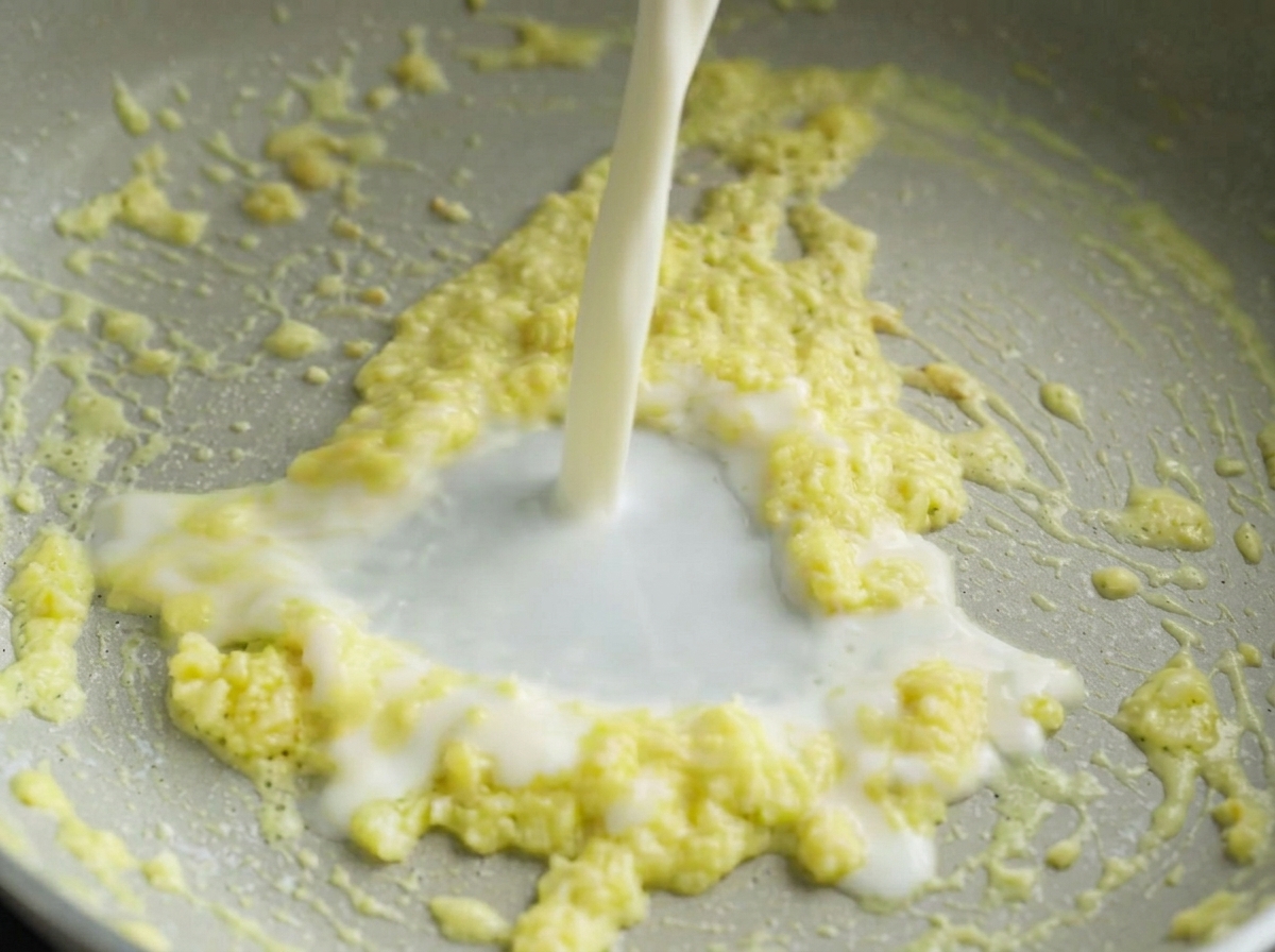 Un filo di latte bianco versato in una padella con burro, amido e aglio.