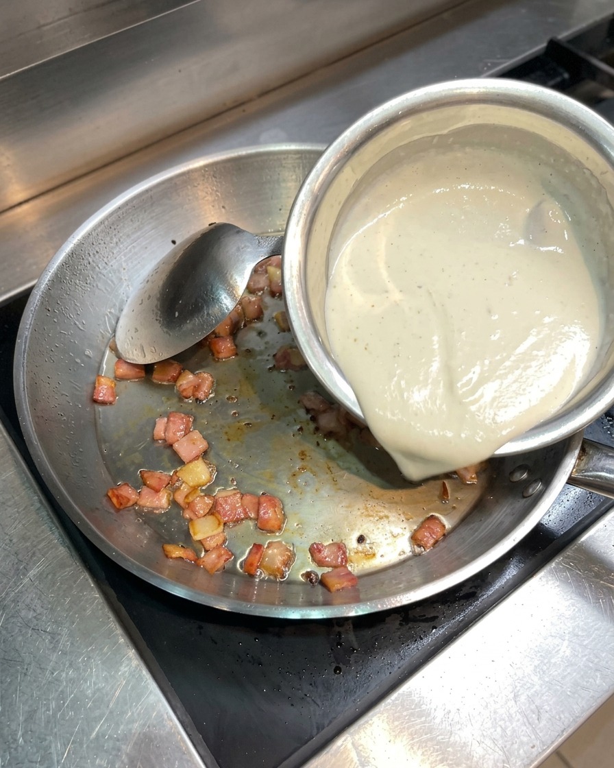 Panna liquida versata da una piccola ciotola in una padella contenente pancetta croccante.