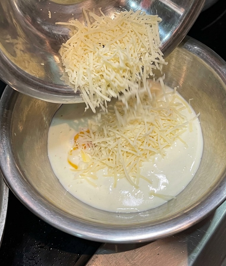 Formaggio grattugiato che cade in un composto di panna e tuorlo duovo.