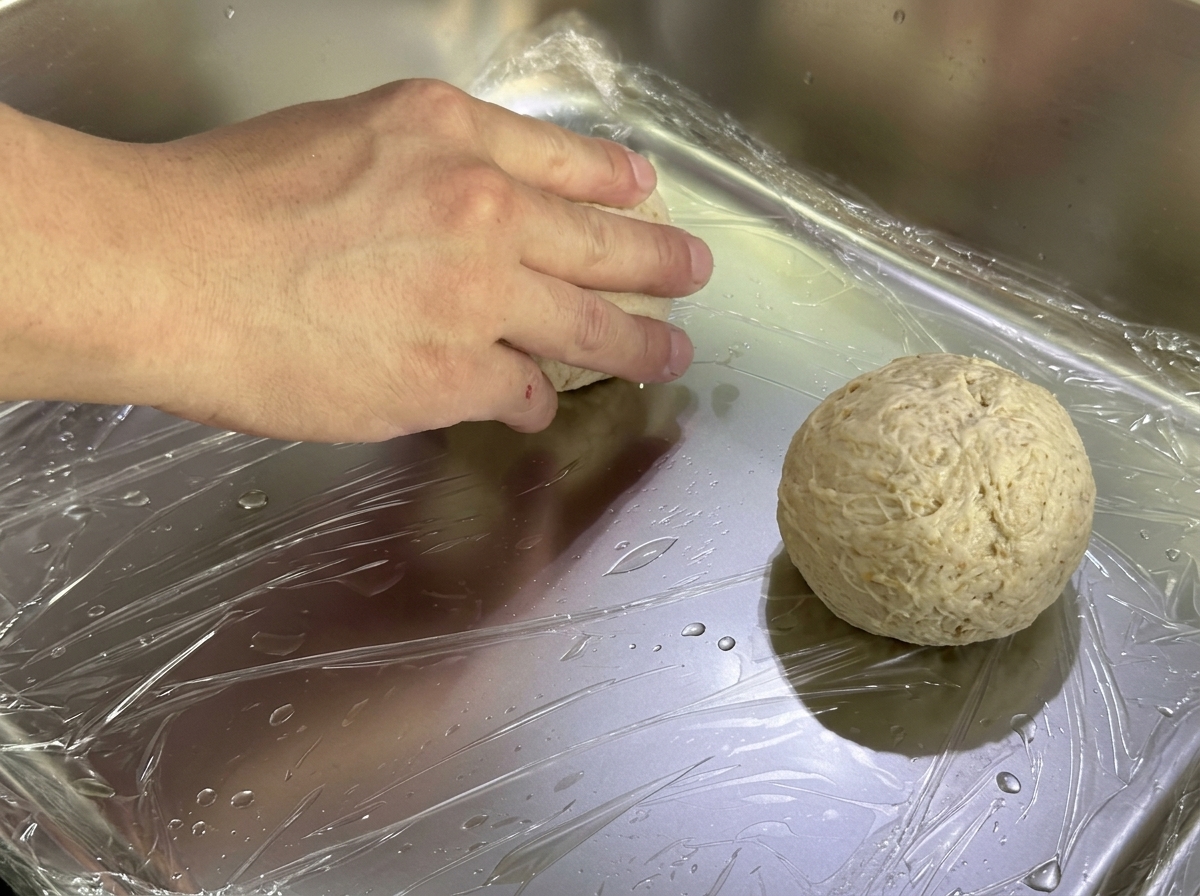 Panetti di impasto su una teglia di metallo coperta con pellicola trasparente per la lievitazione.
