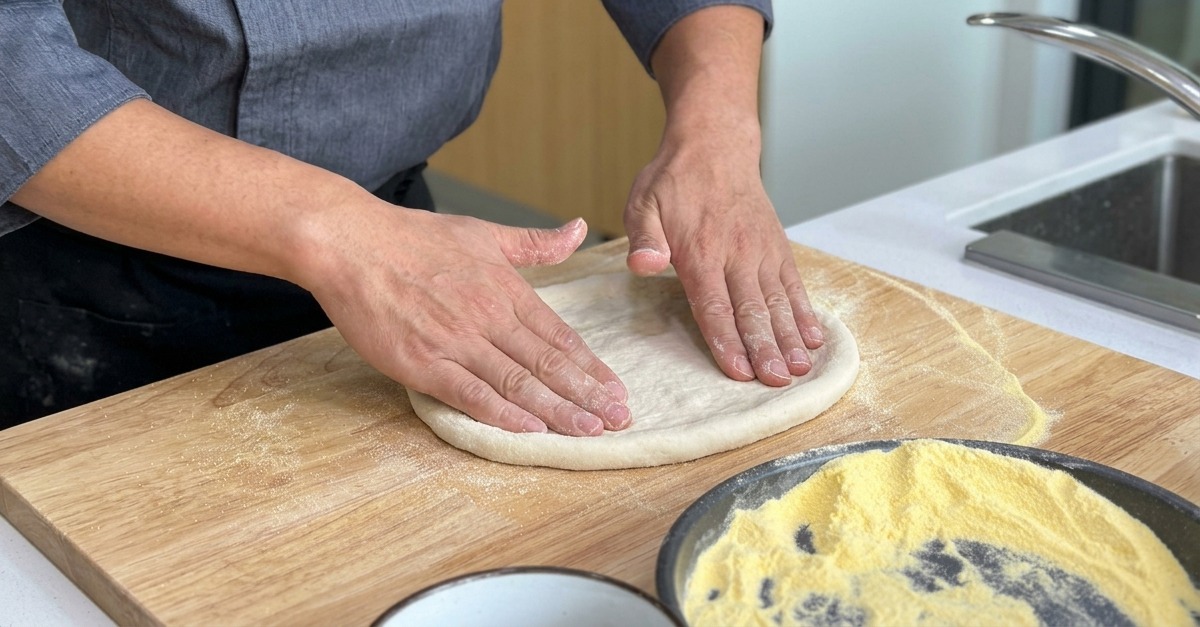 Stesura della base della pizza su un tagliere di legno, mantenendo il bordo rialzato.