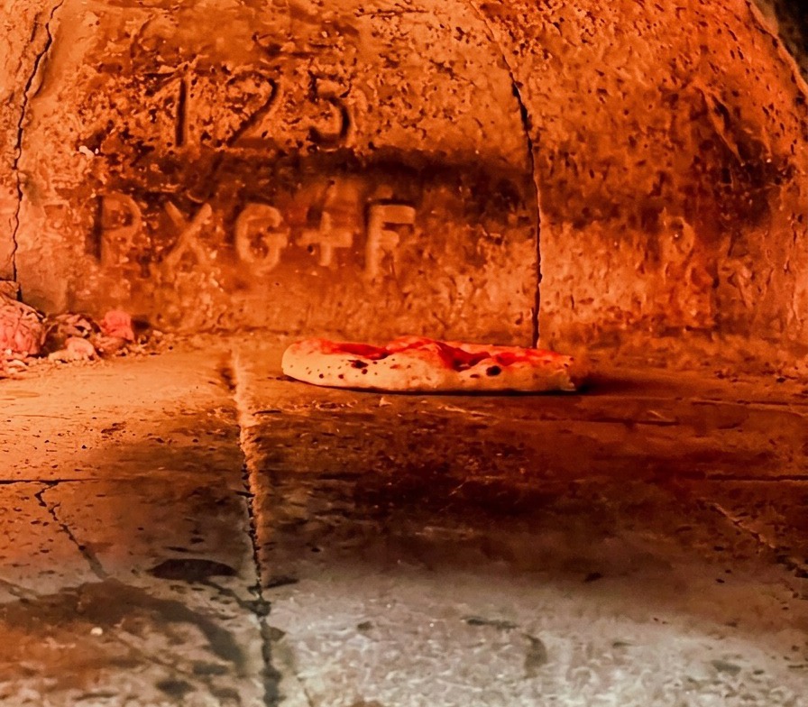 Pizza napoletana che cuoce allinterno di un forno a legna rovente con il bordo che inizia a gonfiarsi.