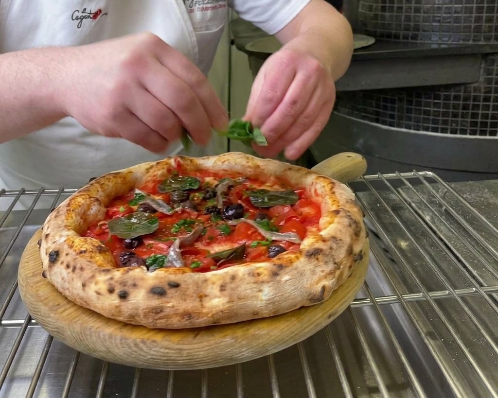 Mani di uno chef che posizionano foglie di basilico verde fresco su una pizza Marinara appena sfornata.