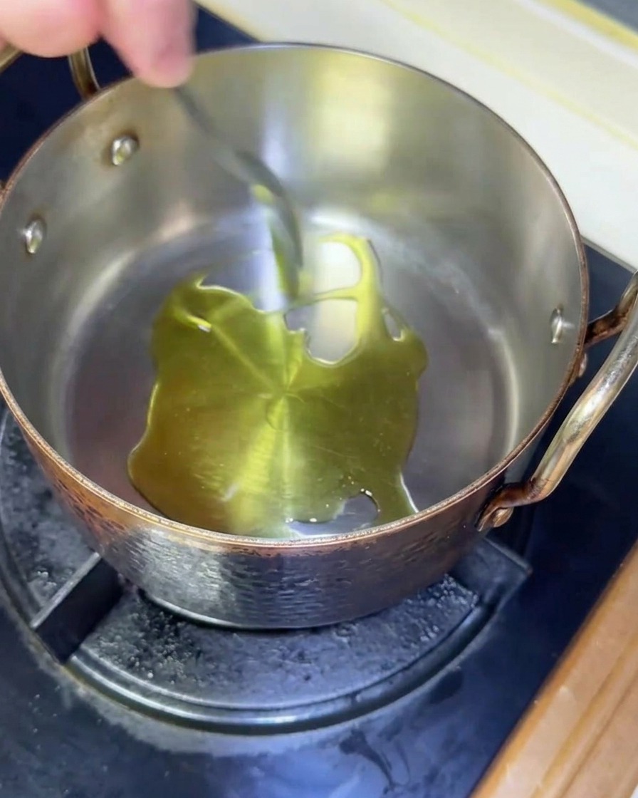 Olio doliva che luccica mentre si scalda in una pentola di rame su un fornello a gas.