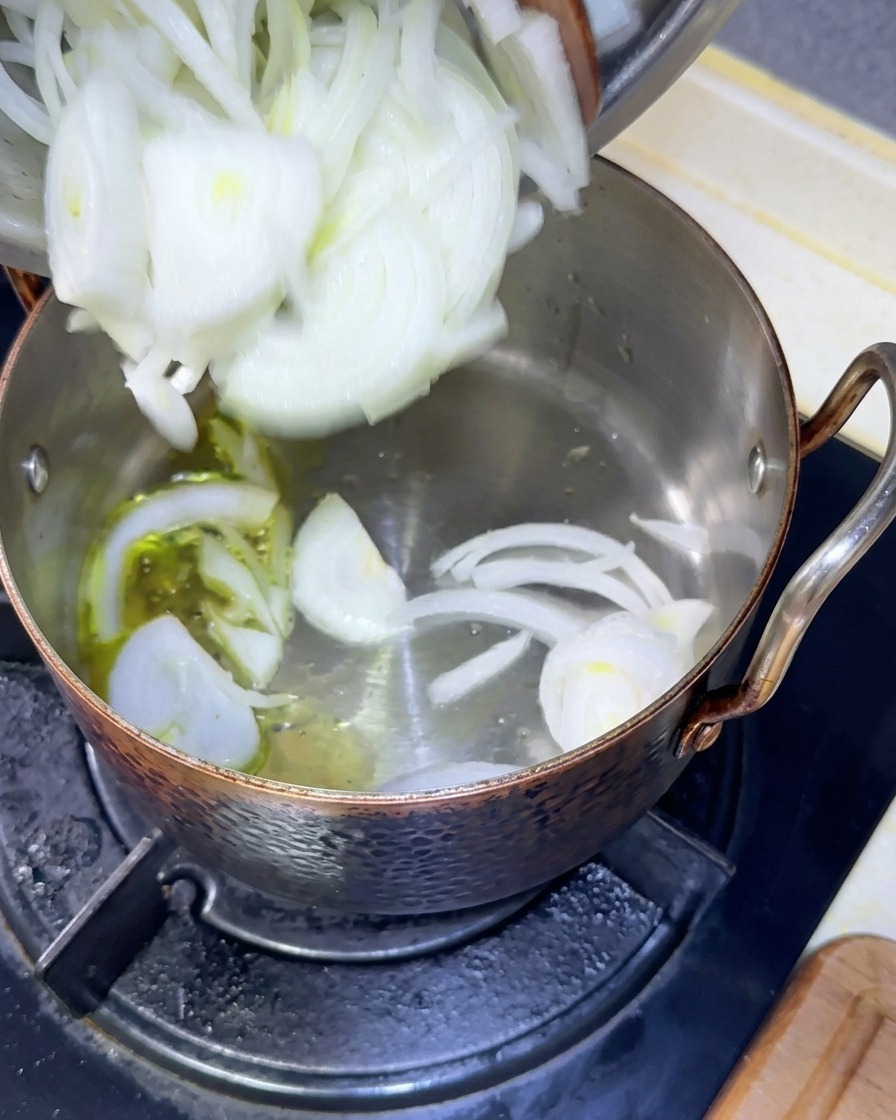 Cipolle bianche appena affettate versate da una ciotola in una pentola con olio caldo.