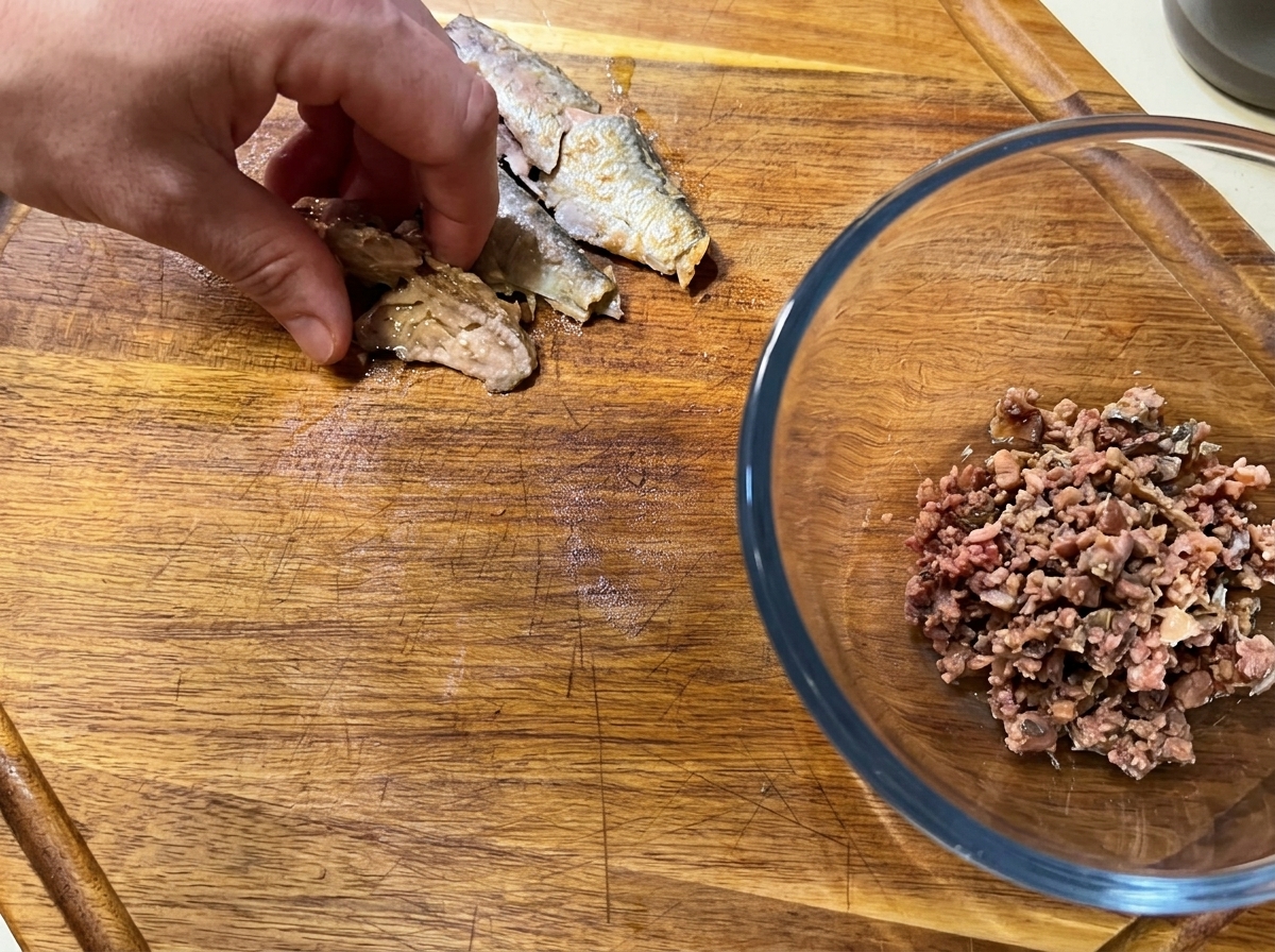 Una mano che spezzetta filetti di sardine diliscate su un tagliere.