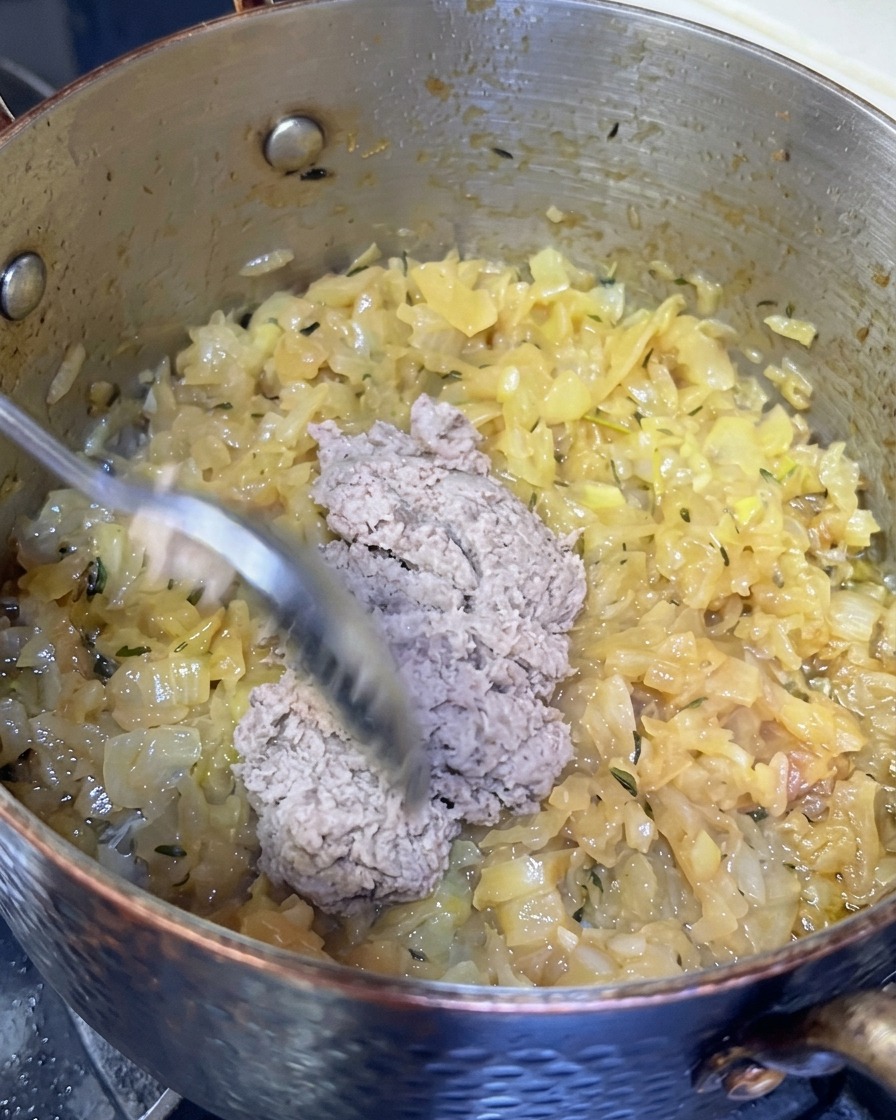 Un cucchiaio di pasta di pesce grigiastra aggiunto a una pentola di cipolle caramellate.