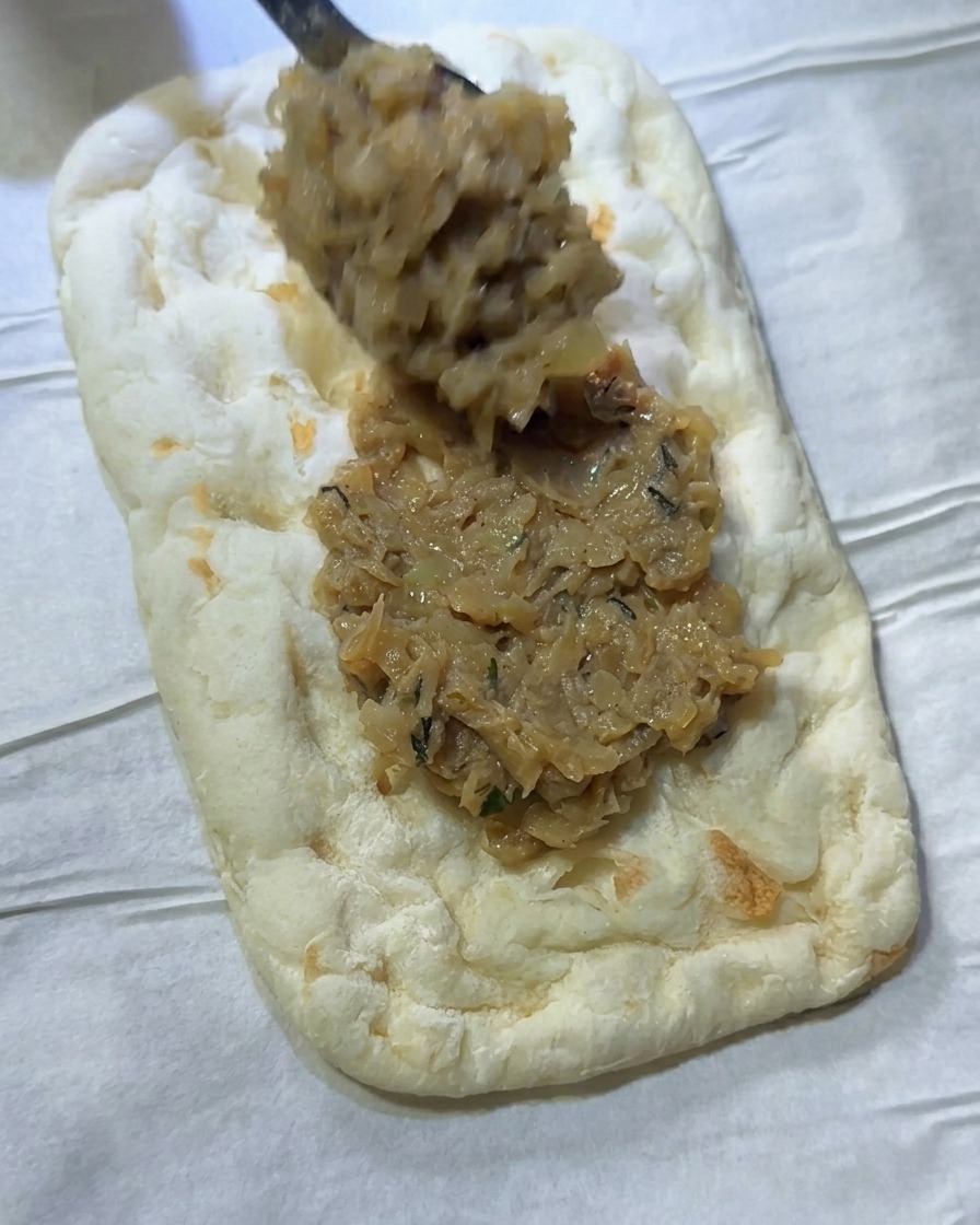 Un cucchiaio di condimento alle cipolle spalmato su un rettangolo di pasta per focaccia.