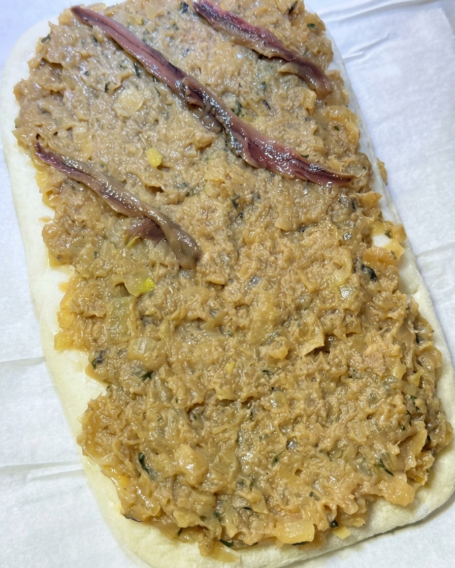 Filetti di acciughe disposti a rombi sopra lo strato di cipolle sulla pasta.