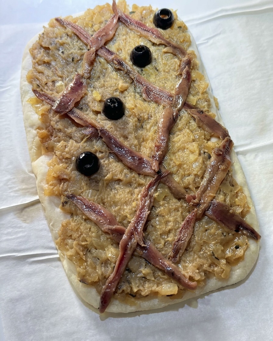 Olive nere intere posizionate al centro dei rombi formati dalle acciughe sulla focaccia.