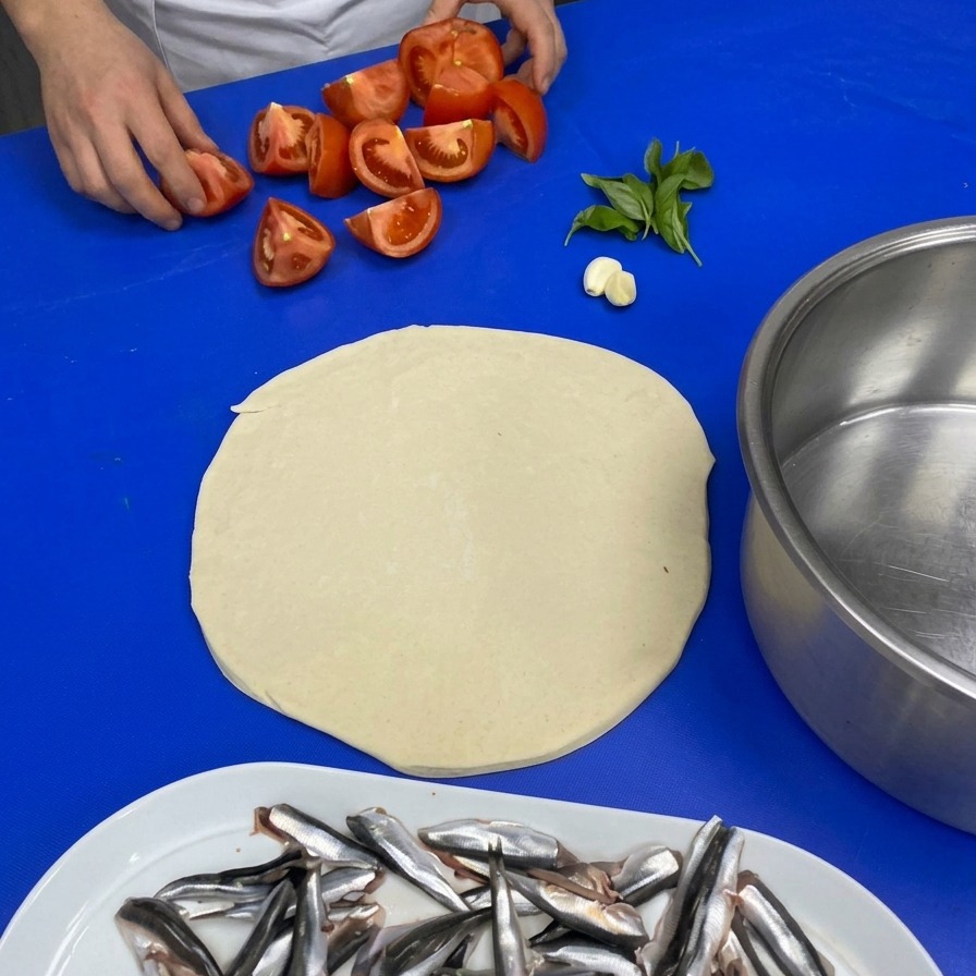 Mani di uno chef che prendono pomodori tagliati da un piano di lavoro insieme ad aglio e basilico fresco.