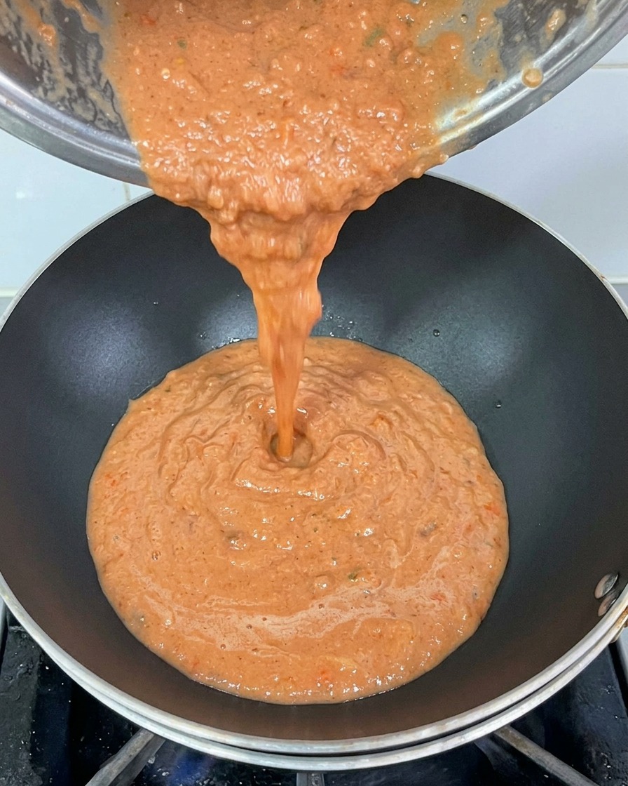 Salsa di pomodoro densa che viene versata da un pentolino in un wok nero ben caldo.