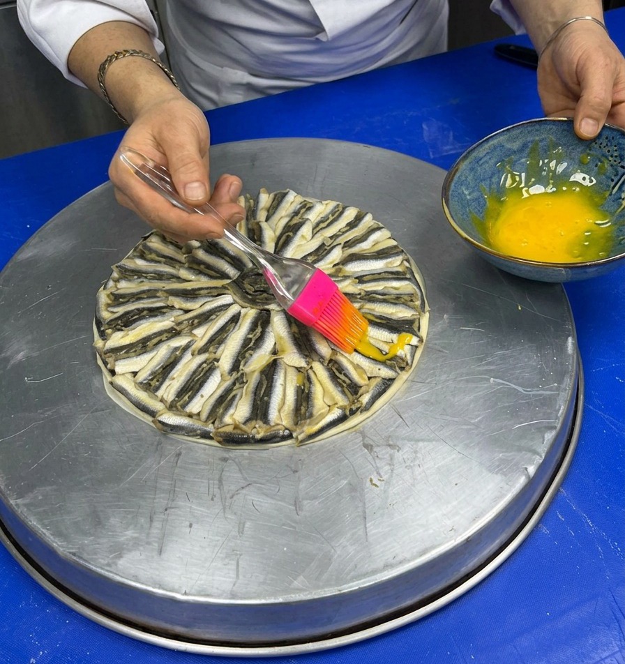 Utilizzo di un pennello in silicone rosa per spennellare il tuorlo duovo sulle alici disposte a raggiera.