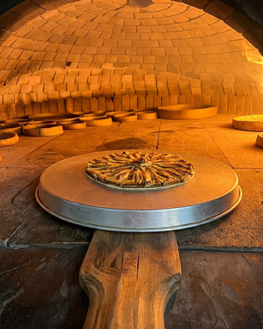 La pizza alle alici su una teglia di metallo mentre cuoce nel vano arancione di un forno a legna in mattoni.