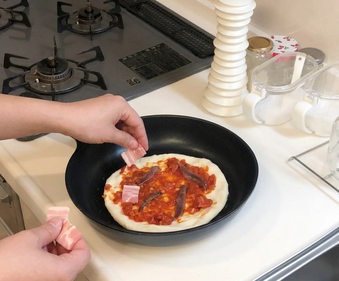 Mani che posizionano pezzetti di pancetta cruda sulla pizza condita con pomodoro e acciughe.