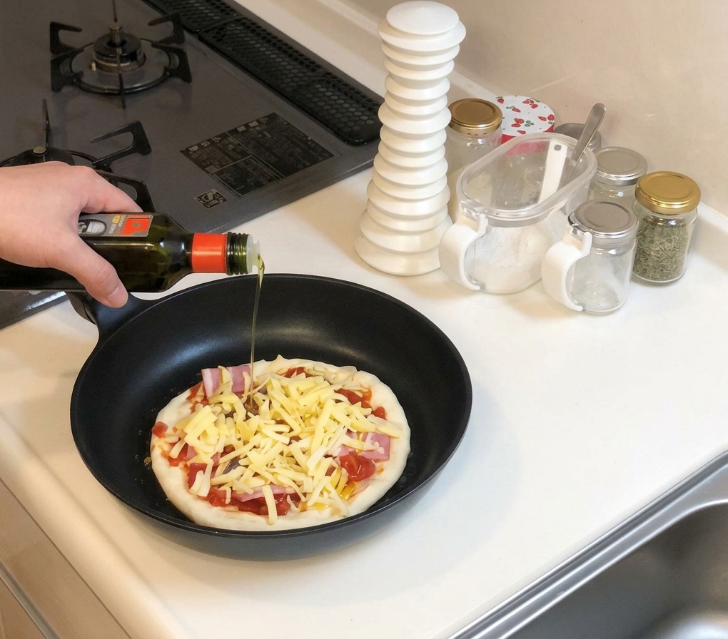 Mano con bottiglia dolio che versa un filo sulla pizza cruda già condita in padella.