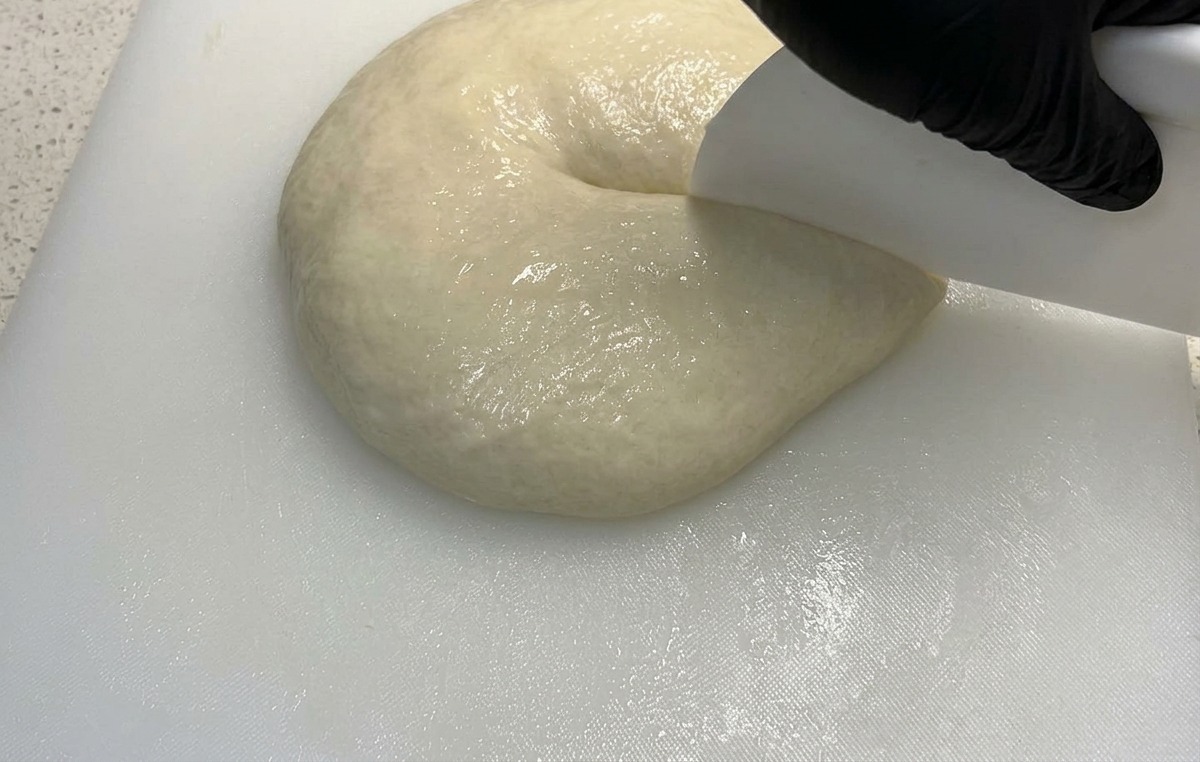 Un raschietto bianco che divide a metà un panetto di impasto soffice.