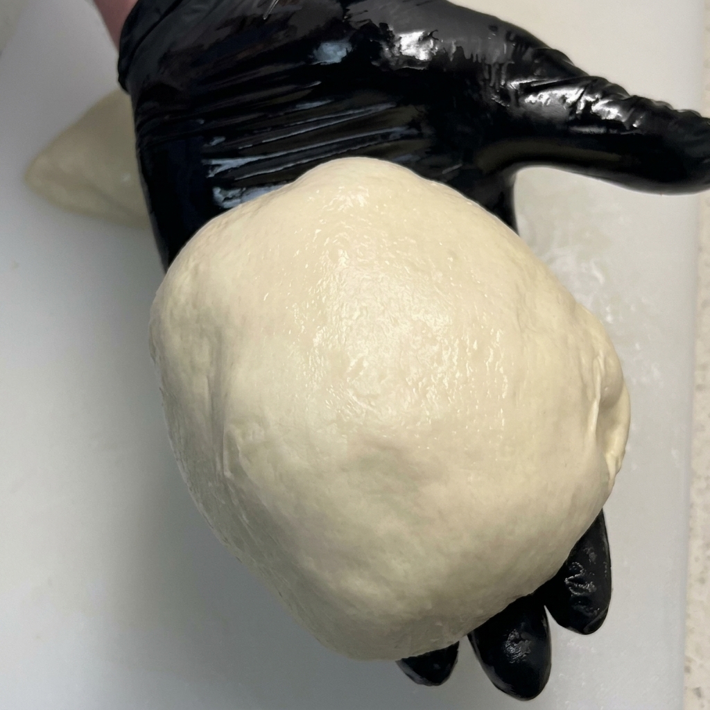 Un panetto di pizza perfettamente liscio e tondo tenuto nel palmo di una mano.