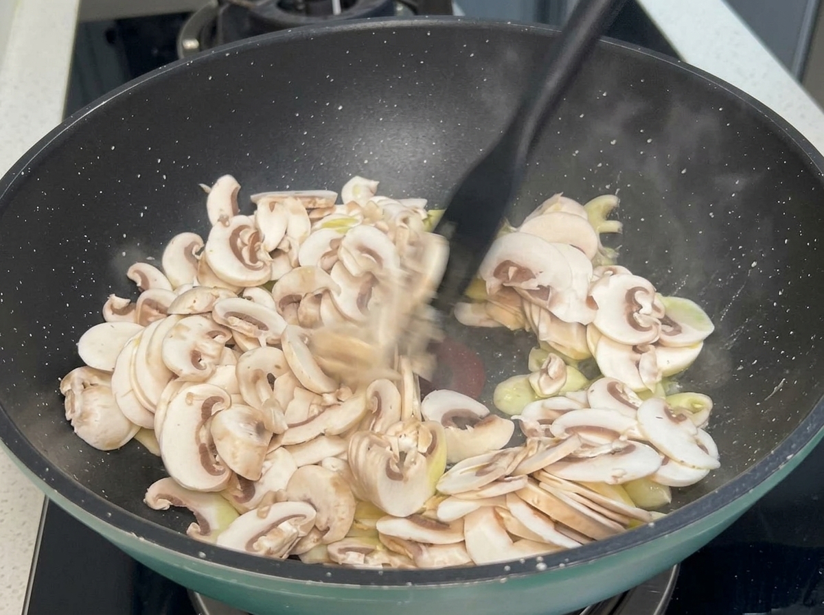 Funghi affettati e aglio che saltano in una padella calda con una spatola nera.