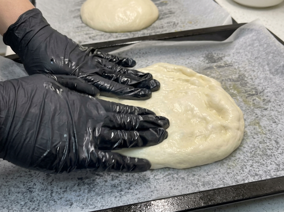 Mani che premono e stendono limpasto della pizza su una teglia con carta forno.