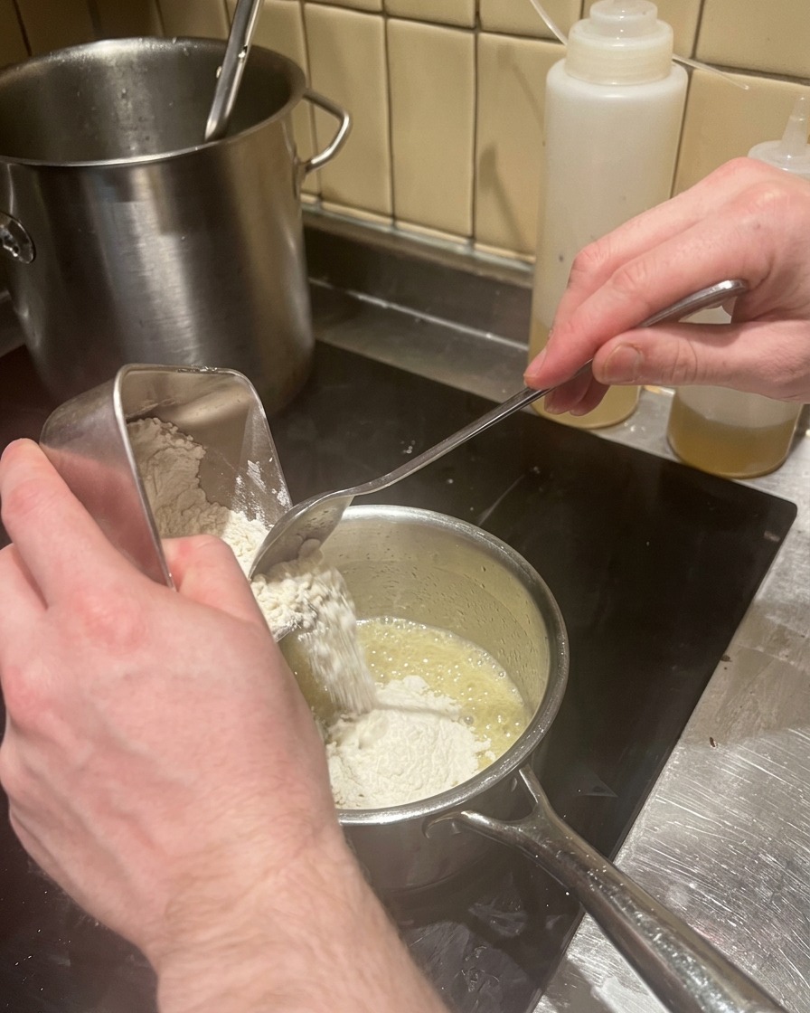 Aggiunta di farina al burro fuso in un pentolino per preparare il roux.