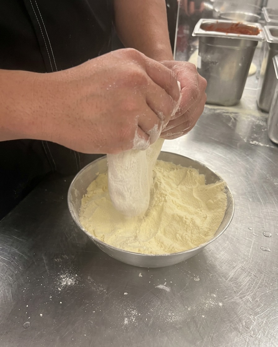 Mani che premono e allargano una pallina di impasto per pizza in una ciotola infarinata.