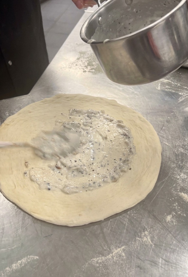 Stesura della crema bianca ai porcini al centro dellimpasto per pizza con un cucchiaio.