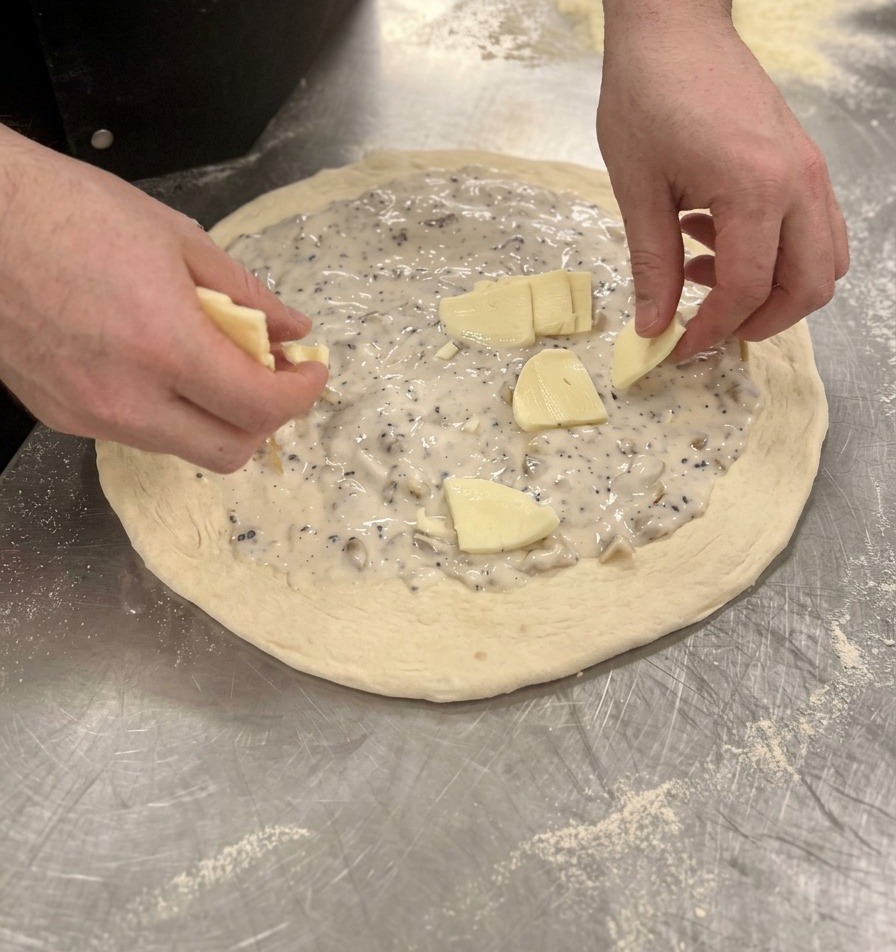 Mani che posizionano pezzetti di mozzarella sulla crema bianca della pizza cruda.
