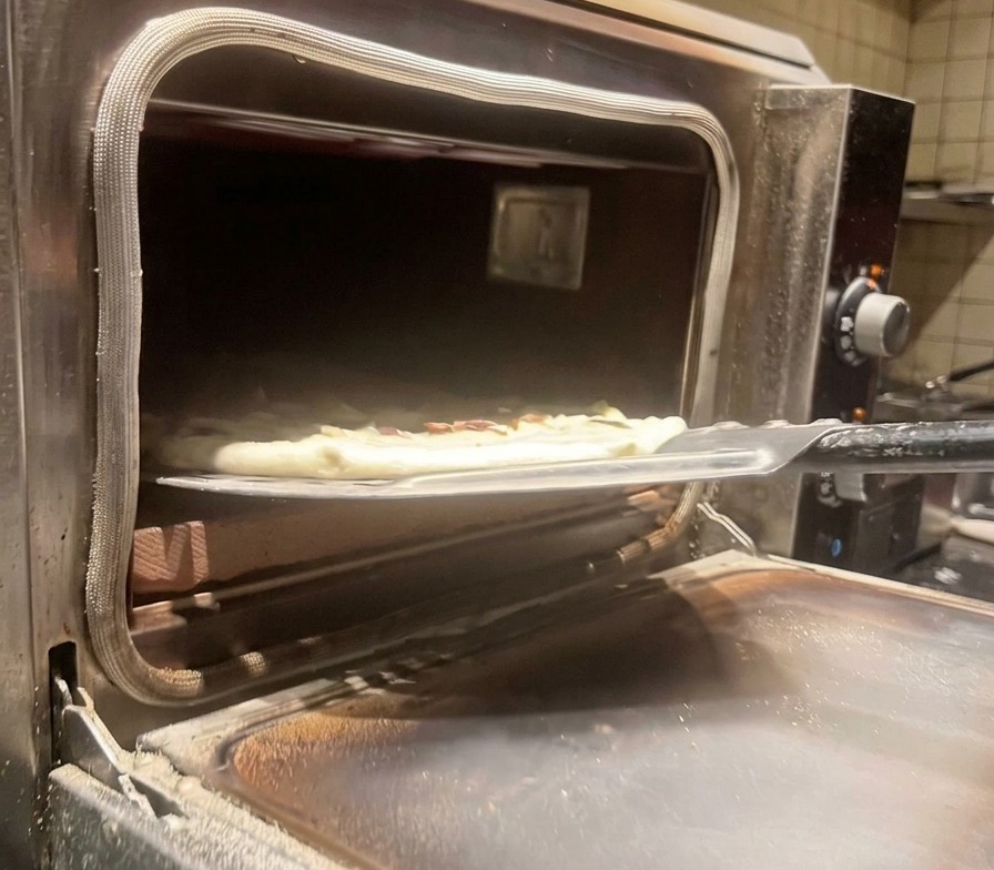Pizza ai funghi cruda infornata in un forno professionale caldo con una pala di metallo.