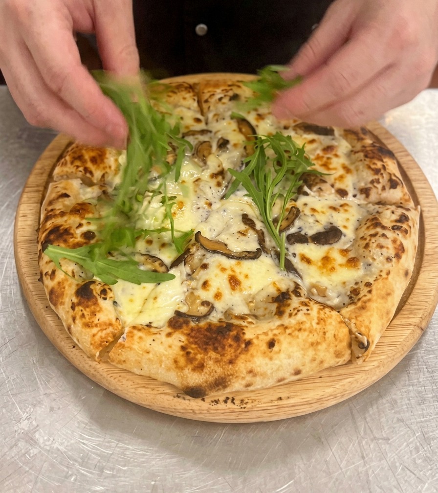 Mani che sistemano foglie di rucola verde brillante sopra la pizza ai funghi tagliata e adagiata su un tagliere di legno.