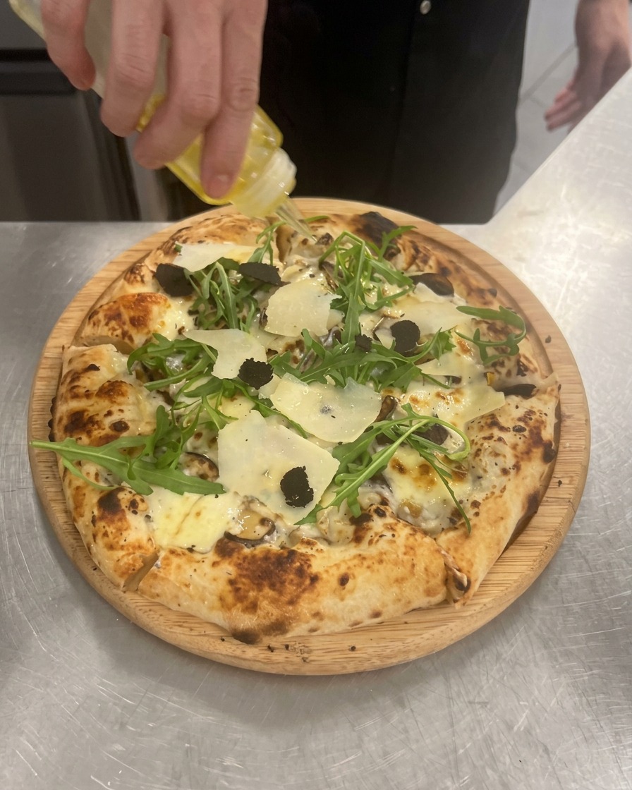 Una mano che spreme una bottiglietta per versare un filo di olio al tartufo dorato sulla pizza finita.