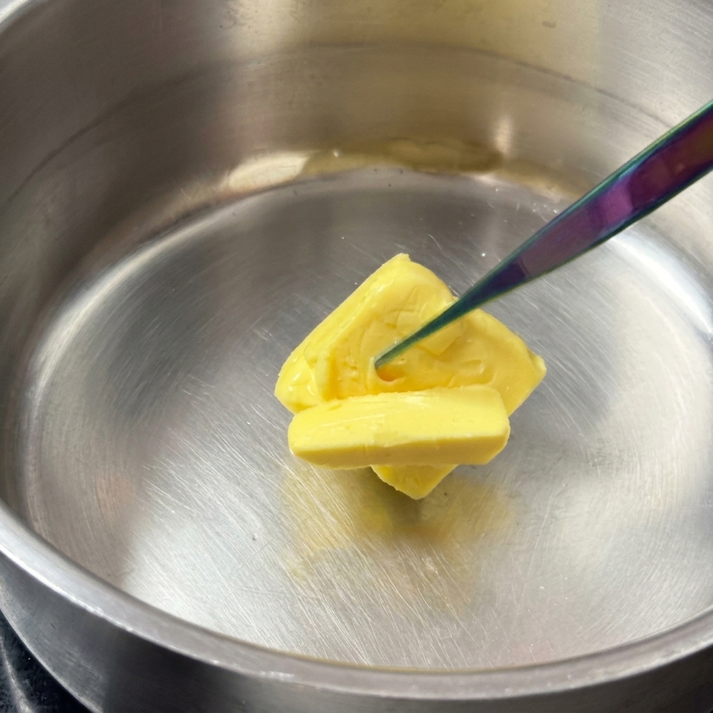 Un panetto di burro giallo che si scioglie in un pentolino di acciaio inossidabile.