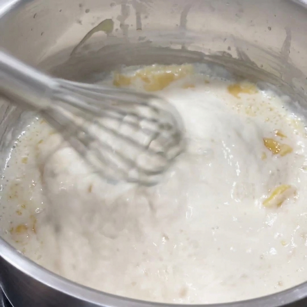 Una frusta che mescola una besciamella densa e spumeggiante in un pentolino.