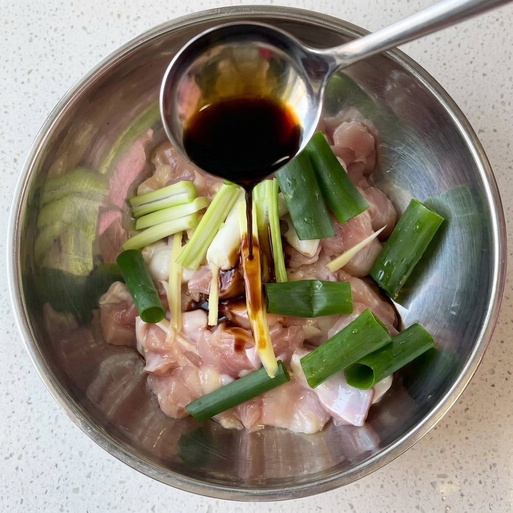 Cubetti di pollo crudo in una ciotola di metallo conditi con salsa di soia, cipollotti e zenzero.