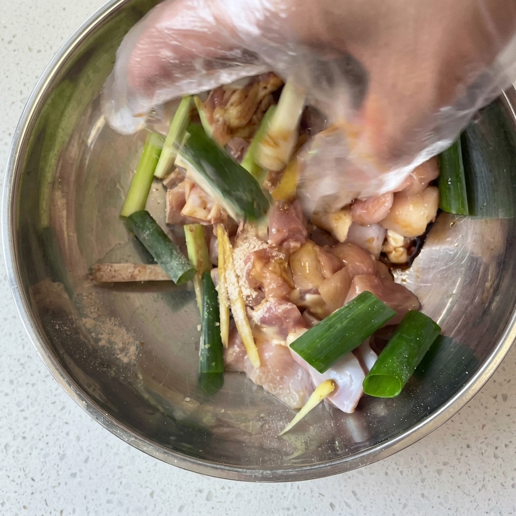 Una mano mescola i pezzi di pollo con la marinata speziata in una ciotola.